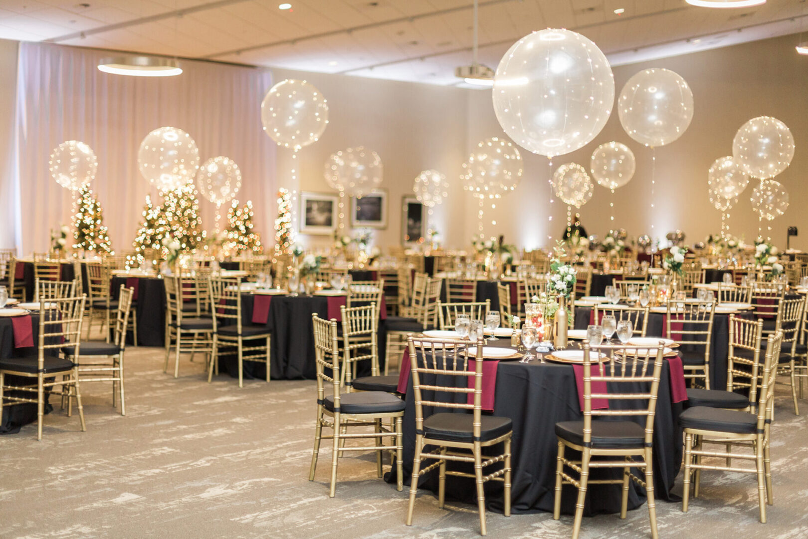 A banquet hall with tables and chairs, balloons hanging from the ceiling.