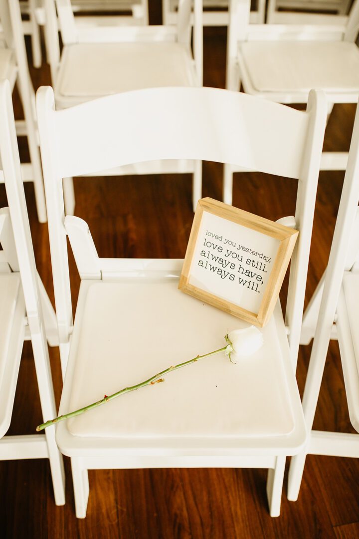 A white chair with a picture frame and a rose.