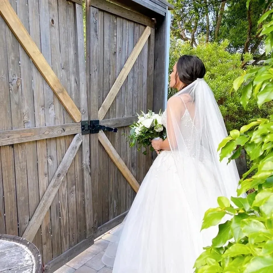 A bride in her wedding dress standing outside of the barn door.
