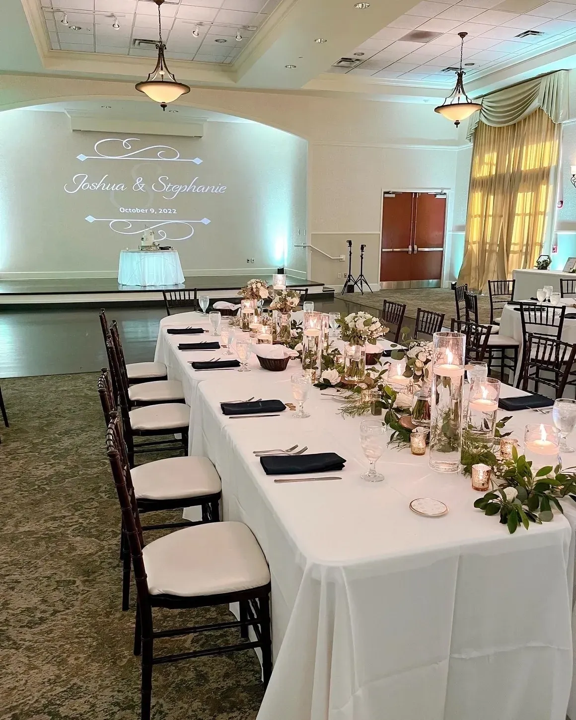 A long table with white linens and black chairs.