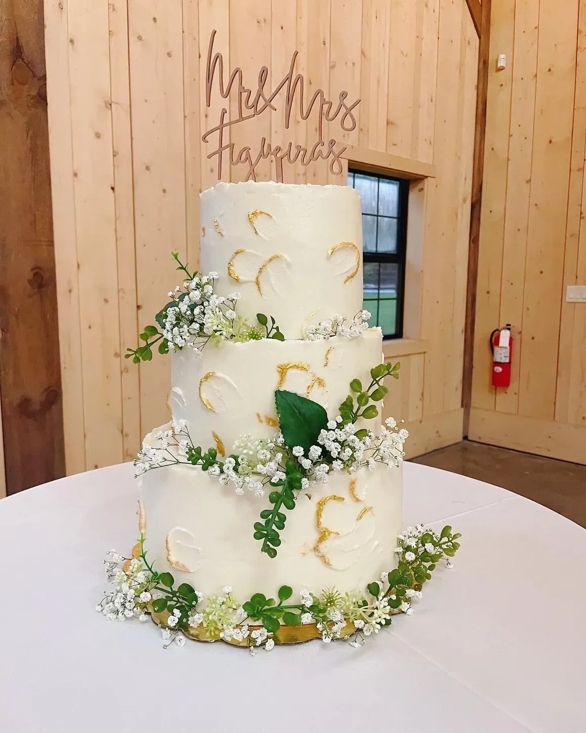 A three layer cake with greenery and flowers on top.